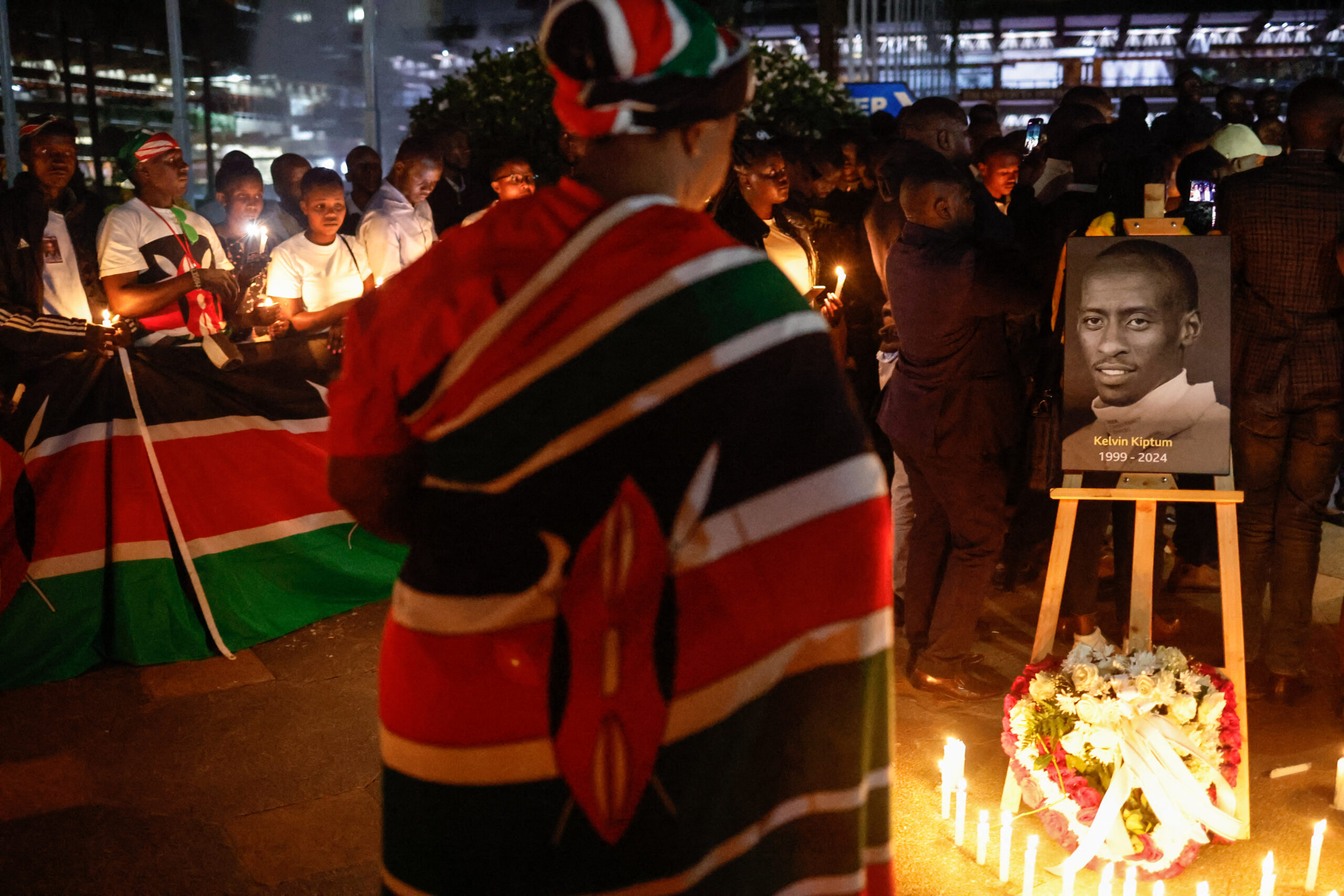A woman wrapped with the national flag of Kenya pays her respect in front of a photo of late Kenyan marathon runner Kelvin Kiptum during a candle light vigil in Nairobi, on February 22, 2024.
